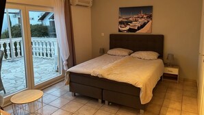 A bedroom with a bed, a nightstand, a lamp, a window with curtains, and a balcony with a railing. - Cozy 2 room apartment with all amenities near krka park (Bilice)