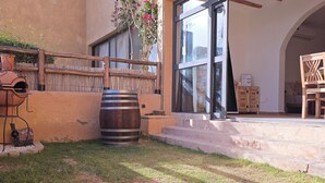 Un edificio con un amplio ventanal, cerca hay una valla de madera y un espacio exterior rústico con un barril y una parrilla.
