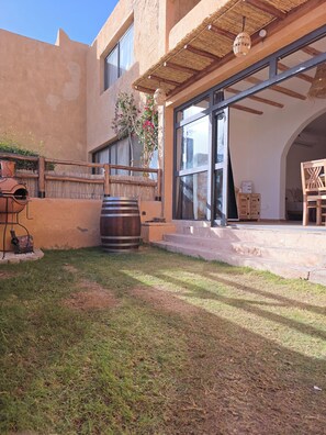 A building with a large glass door, a wooden fence, and a rustic outdoor area with a barrel and a grill. - Taghazout Ait Bihi Cosy short-term accommodation (Ait Bihi)