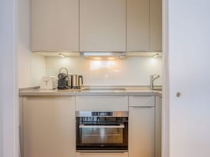 A compact kitchen with a built-in oven, a kettle, and a coffee maker on the countertop.