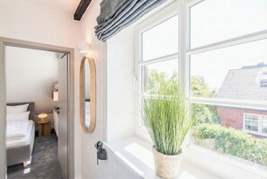 A bedroom with a bed, bedside table, lamp, and a large window with a view of greenery and a building. - Island child 1 - Munkmarsch (Munkmarsch)