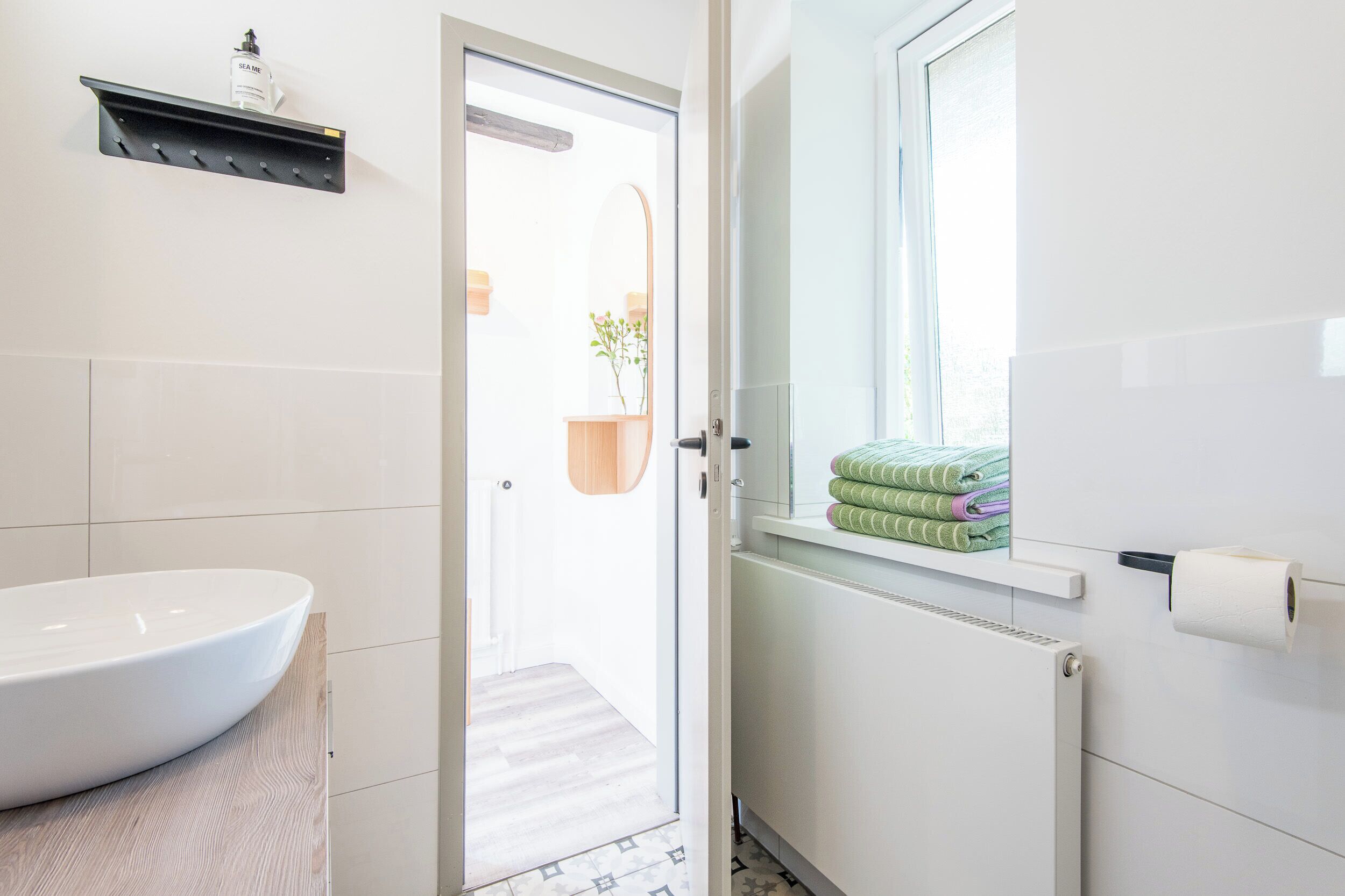 Een badkamer met een wit wastafel, een handdoekhouder met opgevouwen handdoeken, een toiletpapierhouder en een raam met uitzicht.
