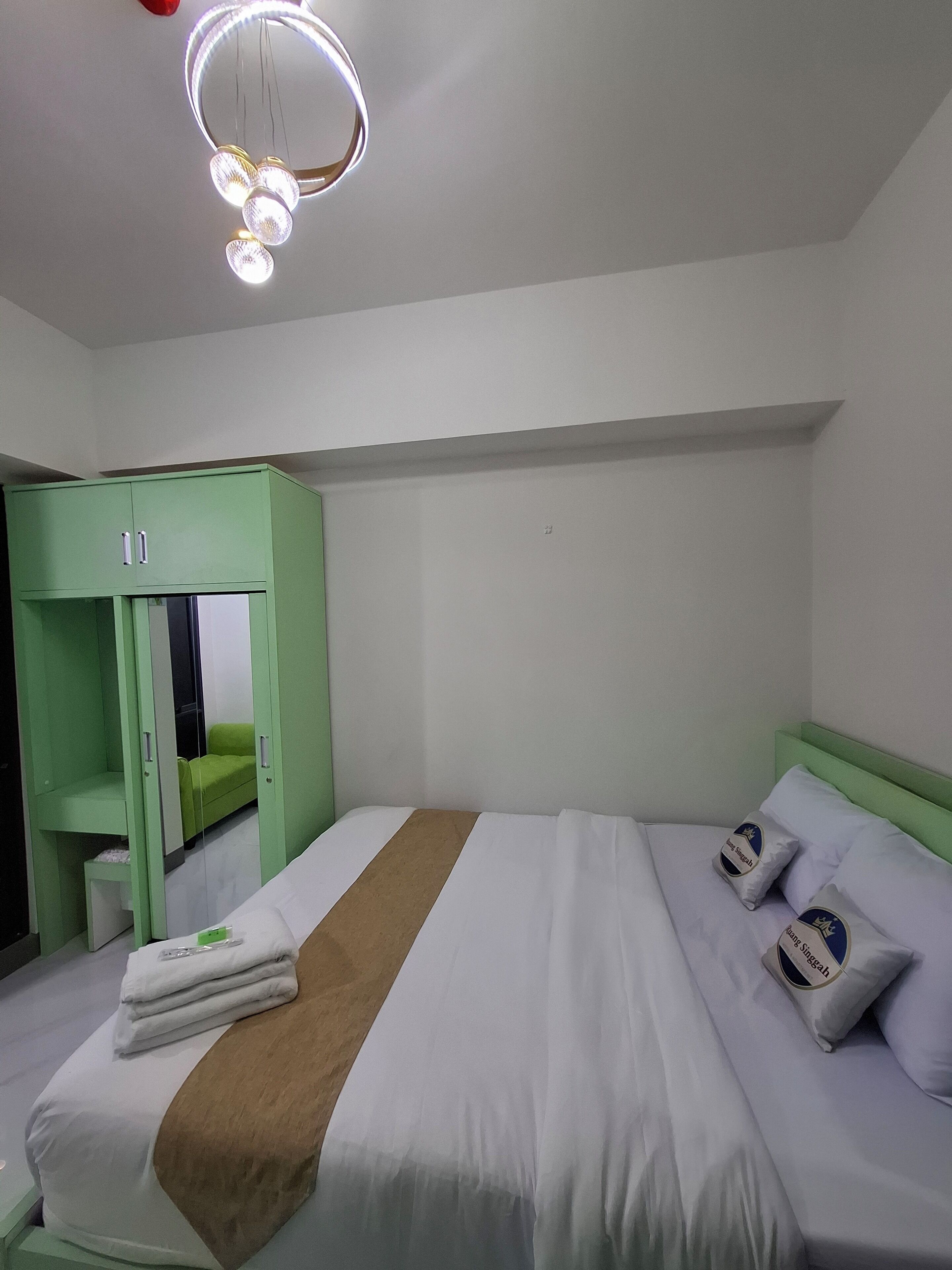 Una habitación de hotel con cama, armario verde y espejo.