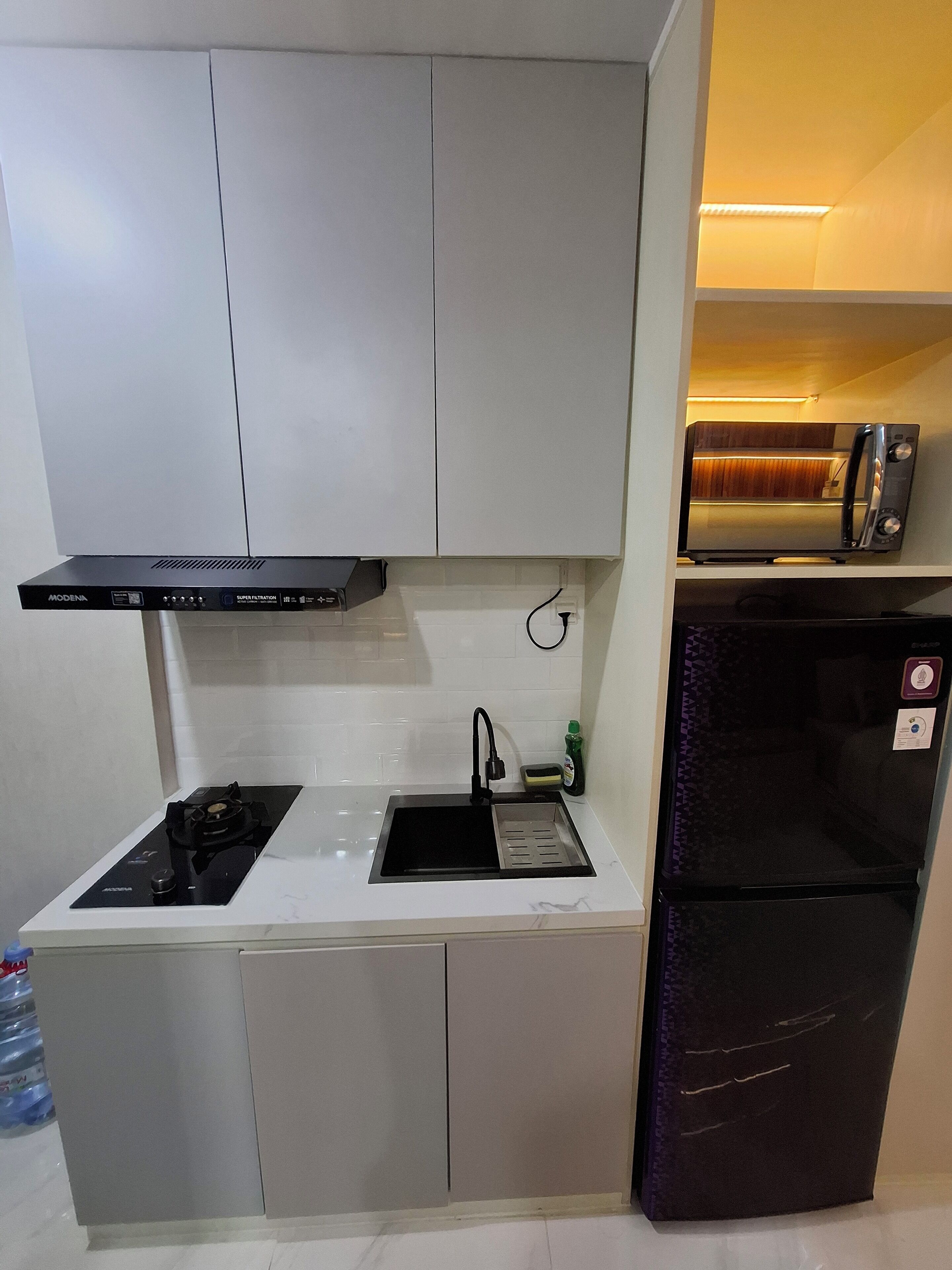 A compact kitchen with a gas stove, a sink, a black refrigerator, and a microwave on a shelf.