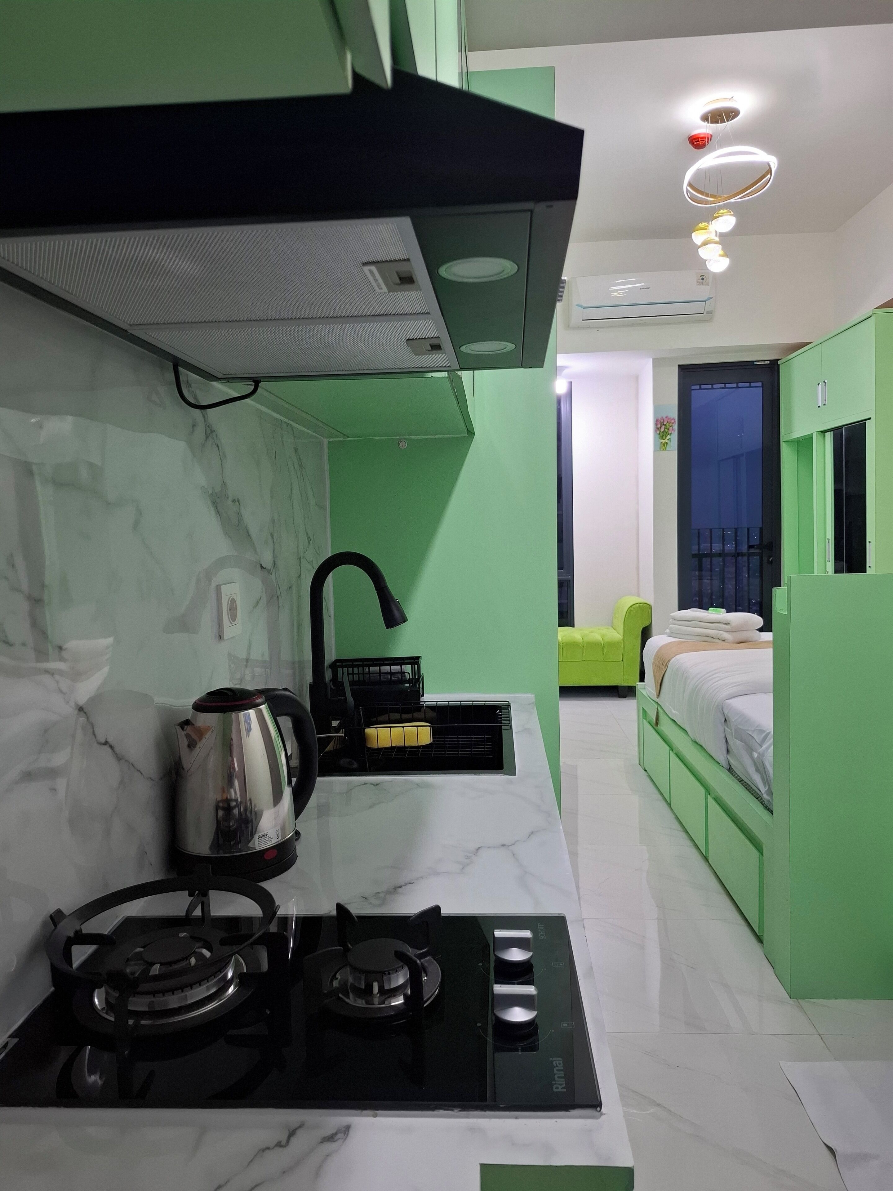 Une cuisine compacte équipée d’une cuisinière à gaz, d’une bouilloire et de luminaires modernes.