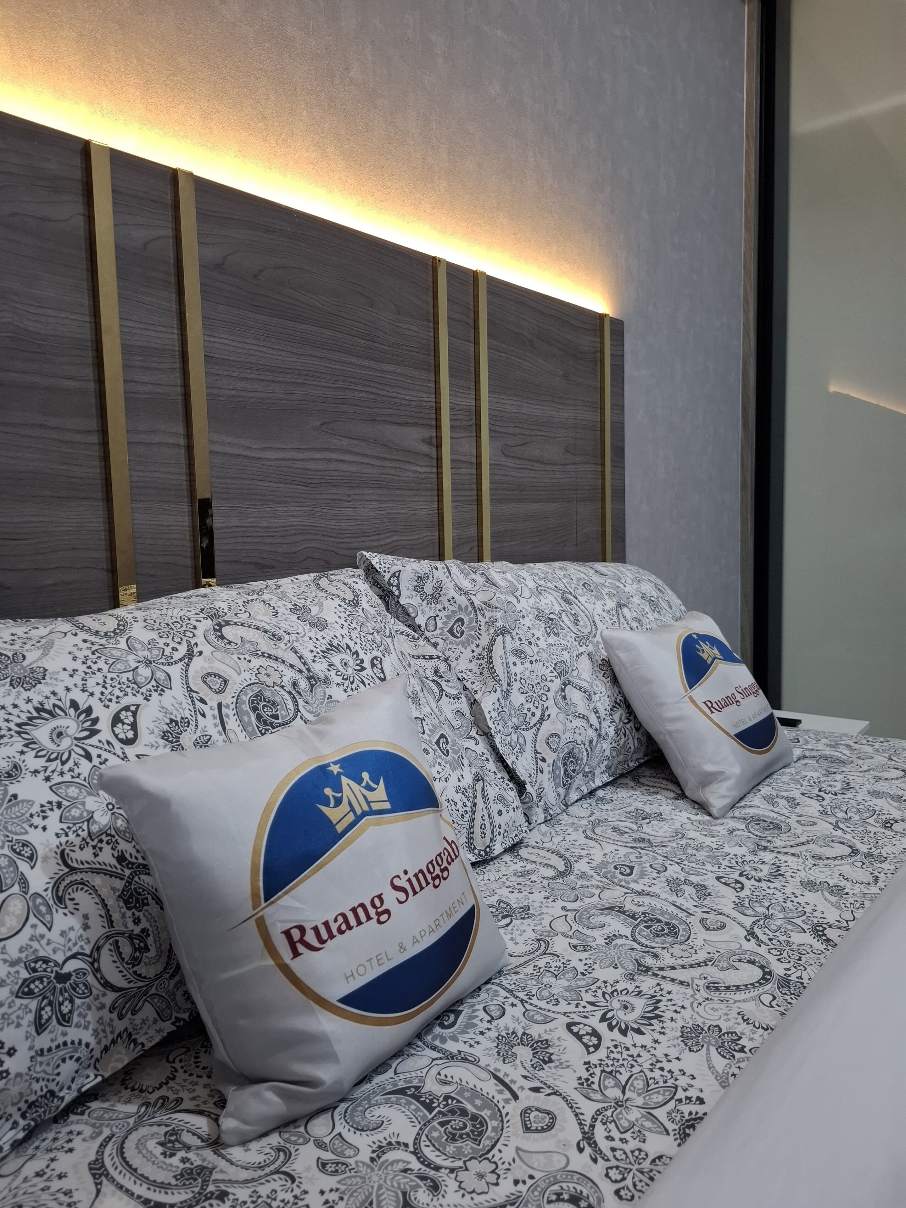 Ein Bett mit gemusterten Bettwäsche und Kissen mit dem Hotel-Logo.