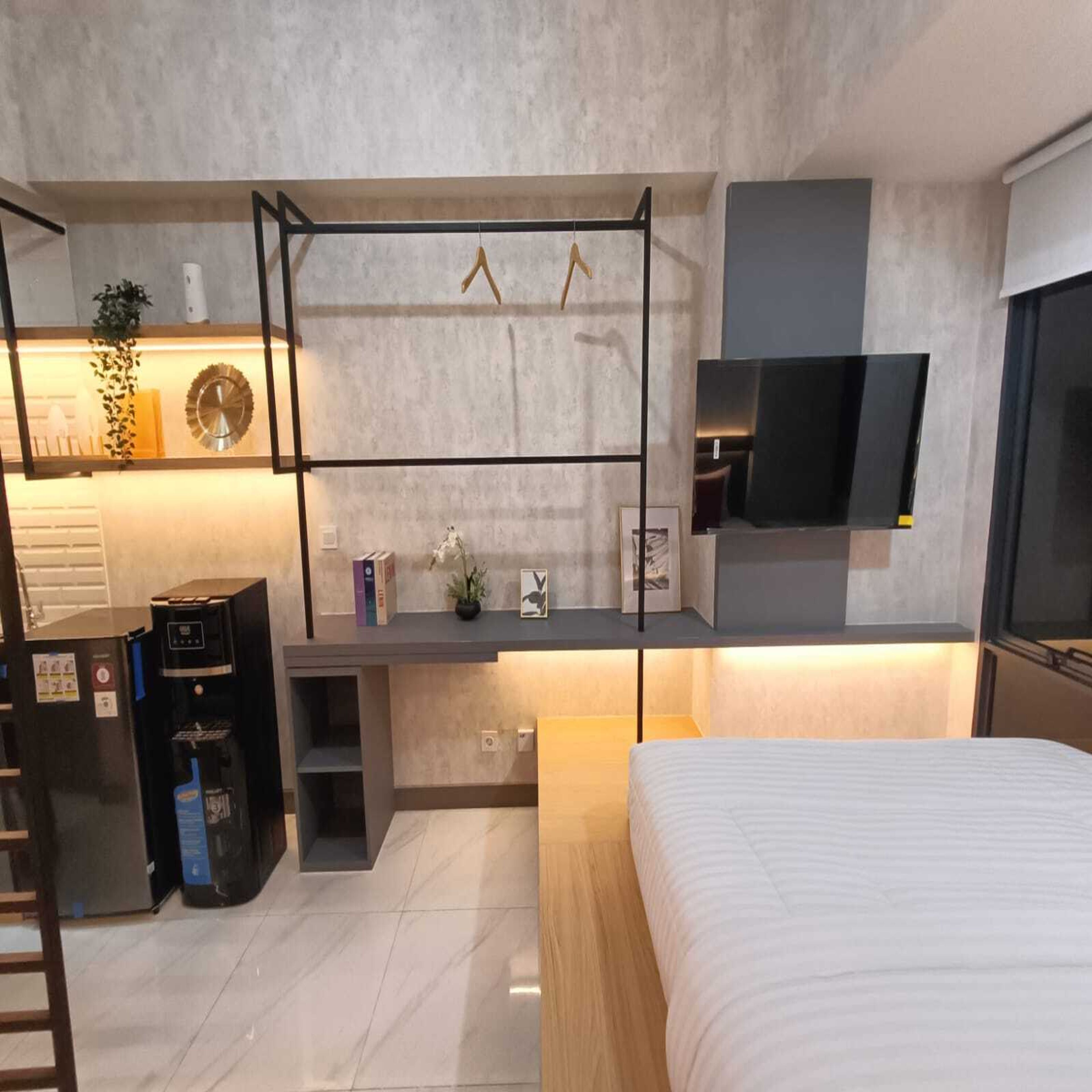 Une chambre moderne comprenant un lit, un bureau avec une télévision, une machine à café et une petite étagère avec des objets décoratifs.
