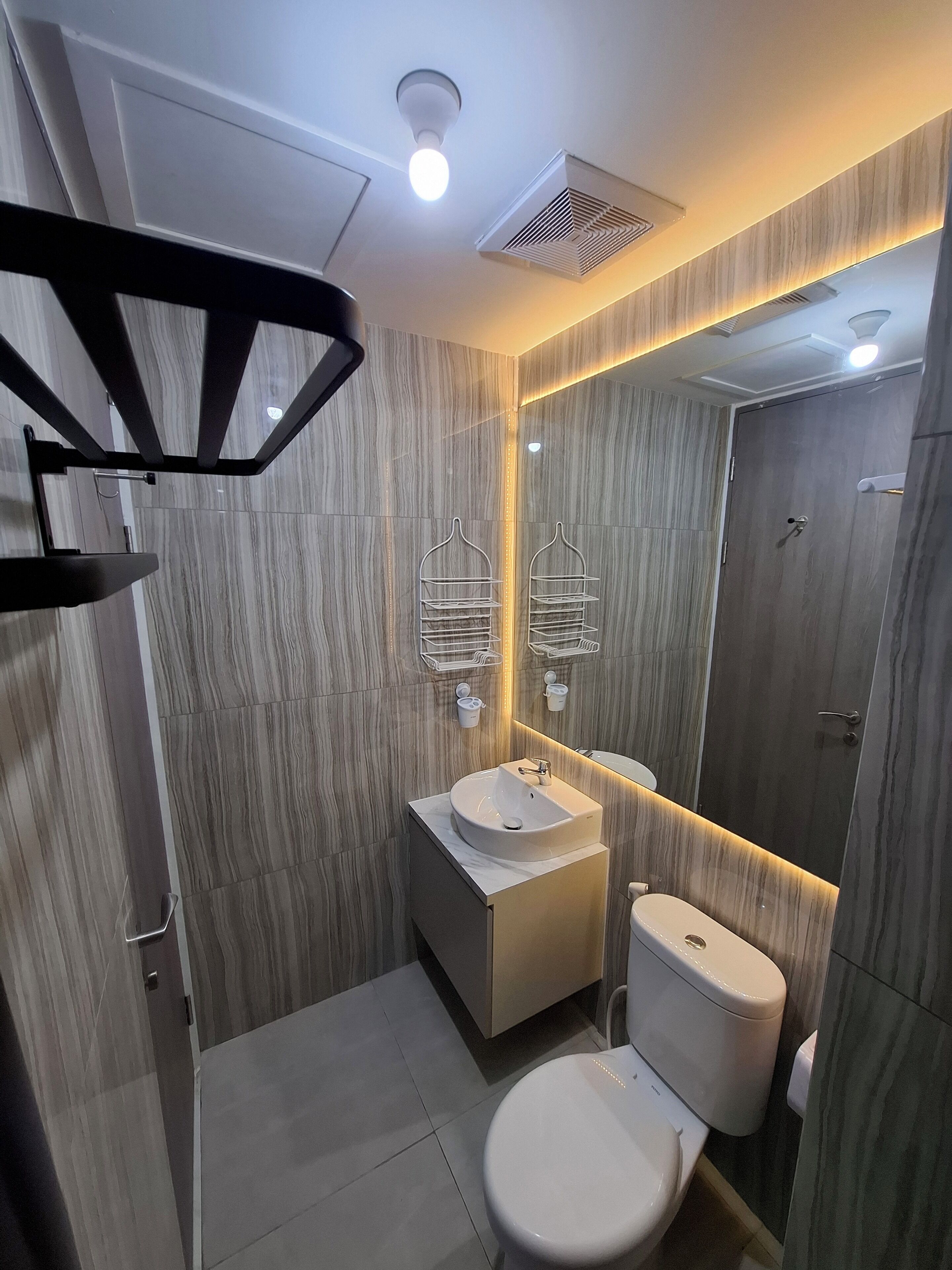 A modern bathroom with a vanity, sink, and toilet. There are two towel racks above the mirror, and a shower area is visible in the background.