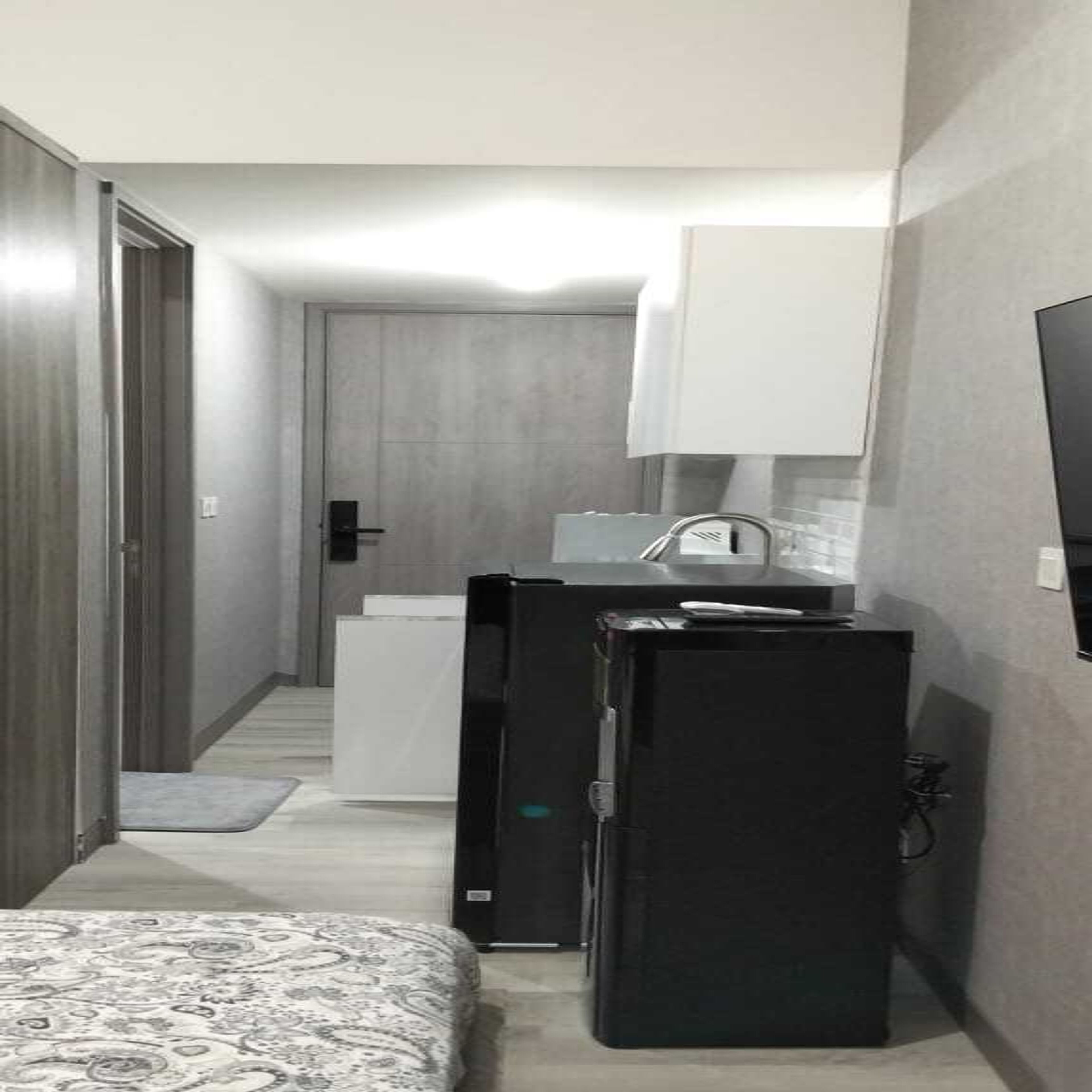 A compact hotel room with a bed, a small kitchenette, and a TV mounted on the wall.