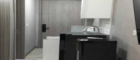 A compact hotel room with a bed, a small kitchenette, and a TV mounted on the wall.
