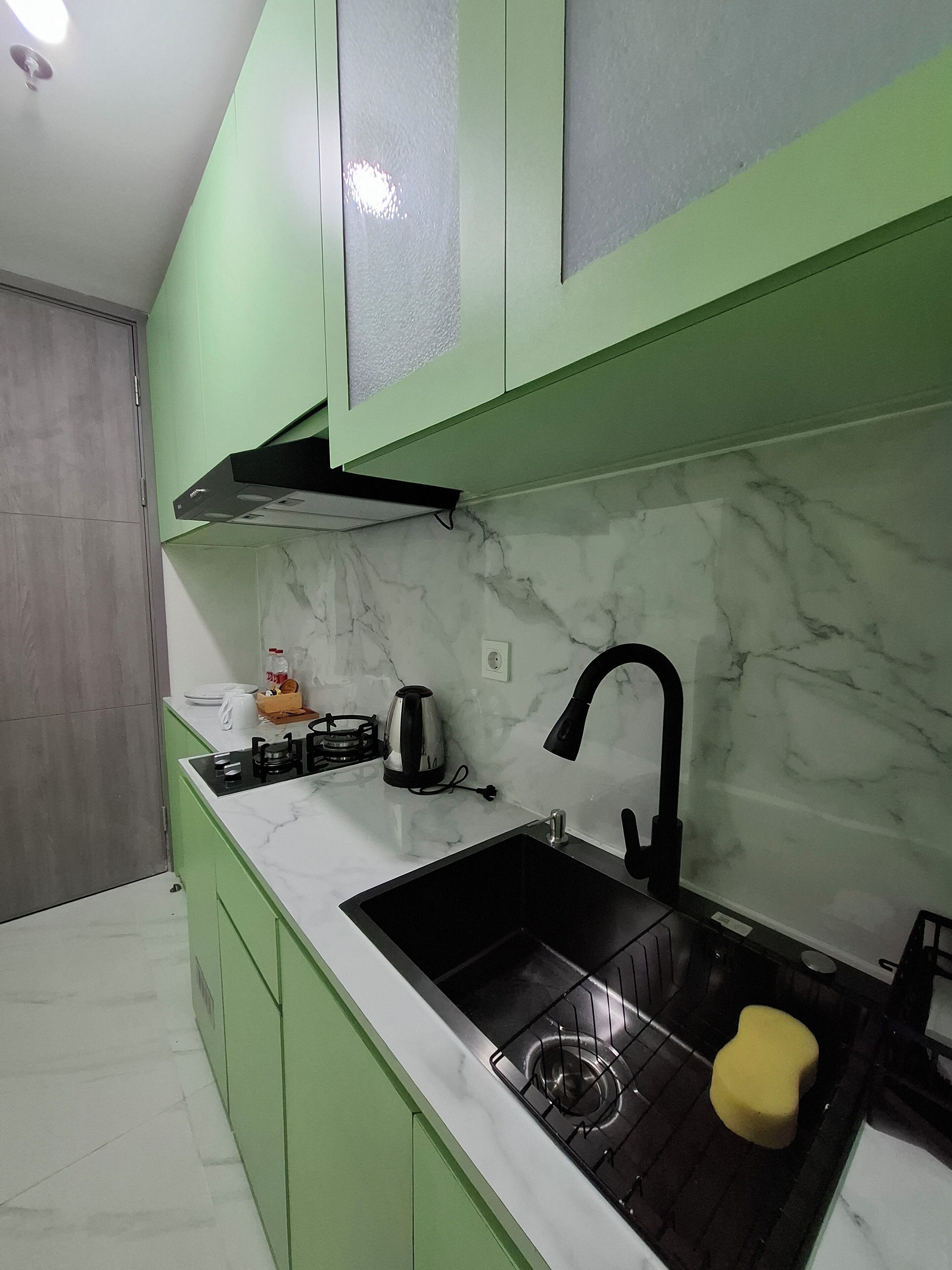 A kitchen with green cabinets, a marble countertop, a black sink, and a yellow sponge.