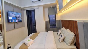A modern hotel room with a large bed, a flat-screen TV mounted on the wall, an air conditioning unit, and a unique ceiling light fixture. - Apartmen Pakuwon Bekasi by Ruang Singgah (Bekasi)