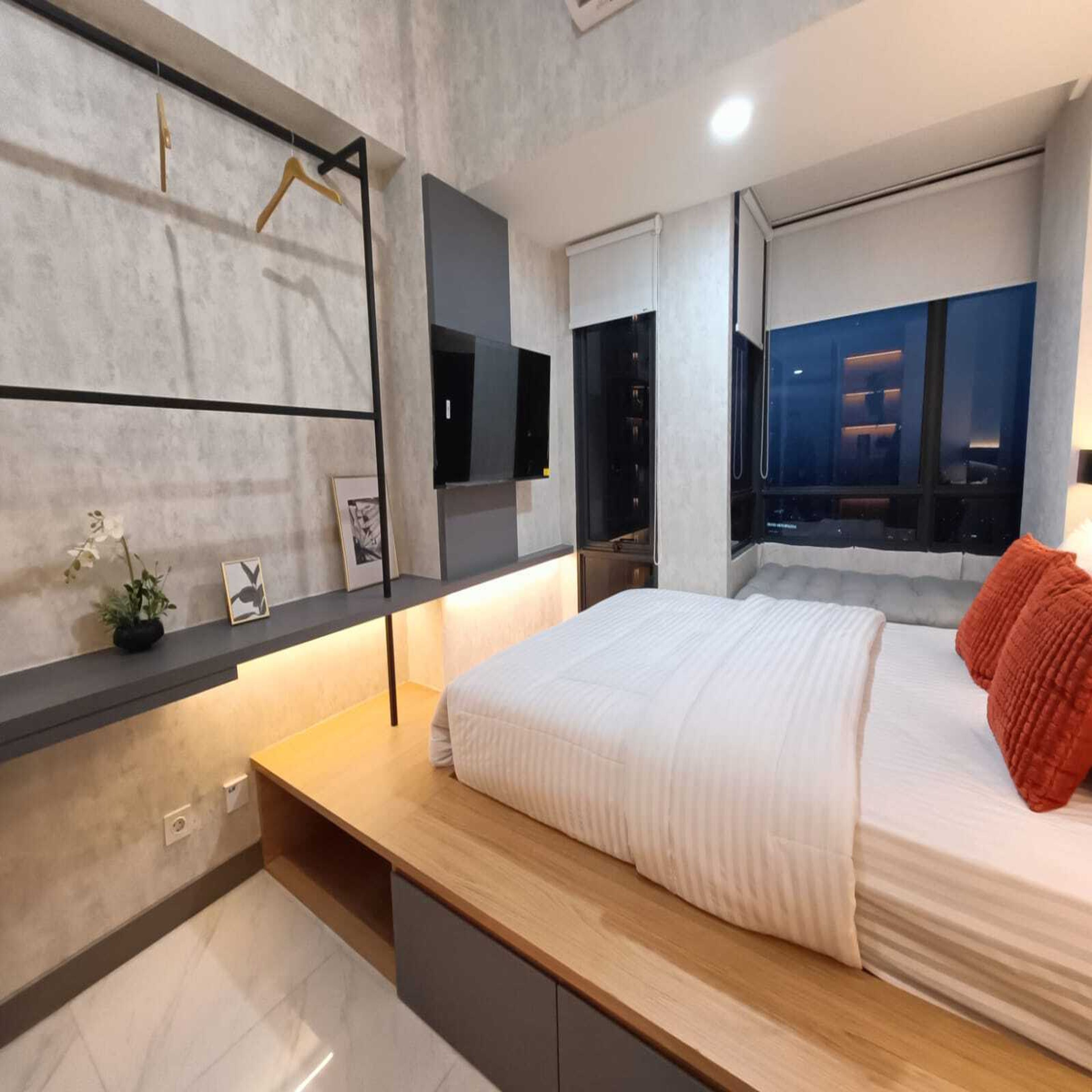 A modern bedroom with a bed, bedside tables, a TV, and a window with a city view.