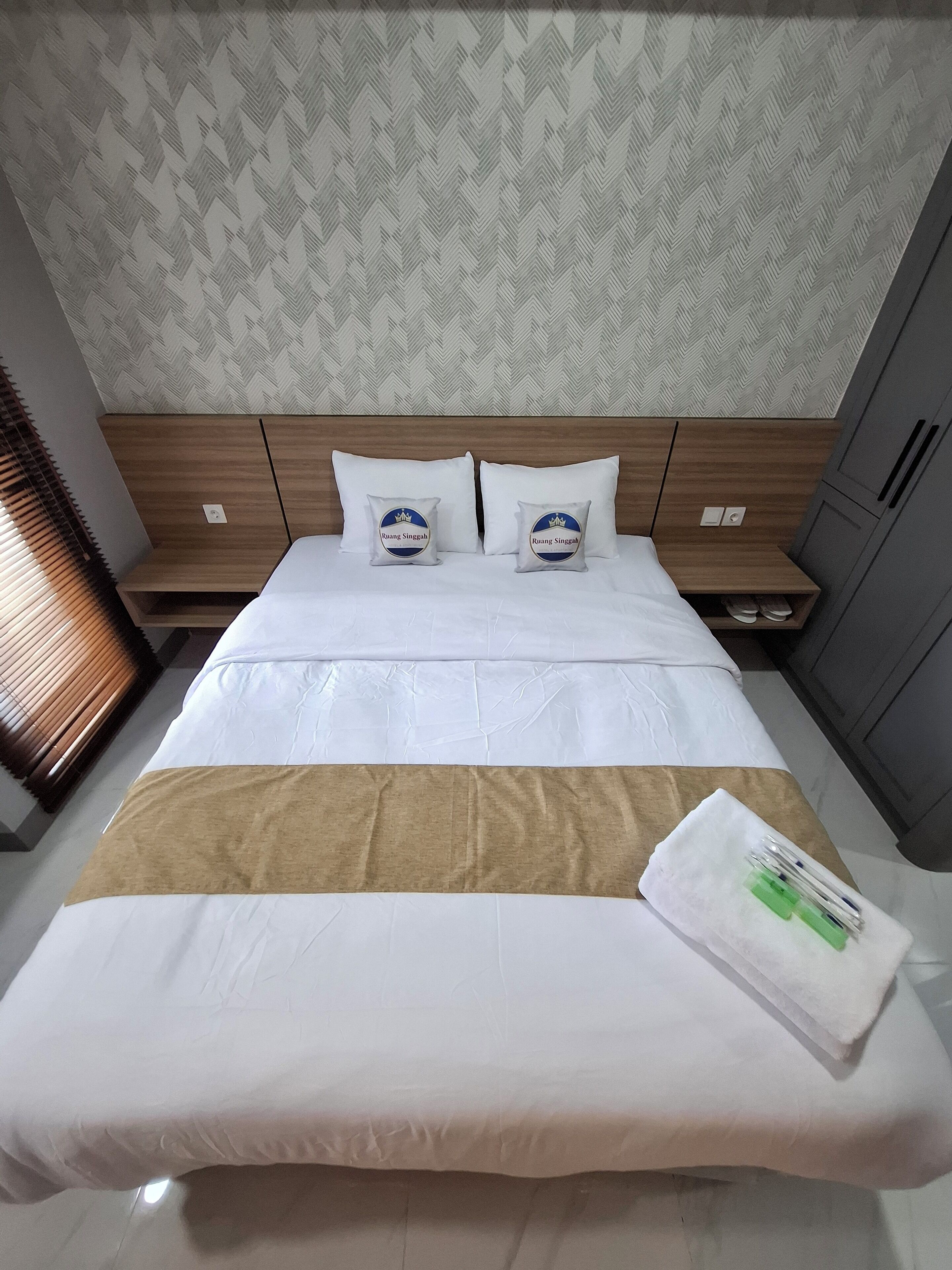 Camera d'albergo con un letto, due cuscini, una testiera in legno, un comodino e un armadio.