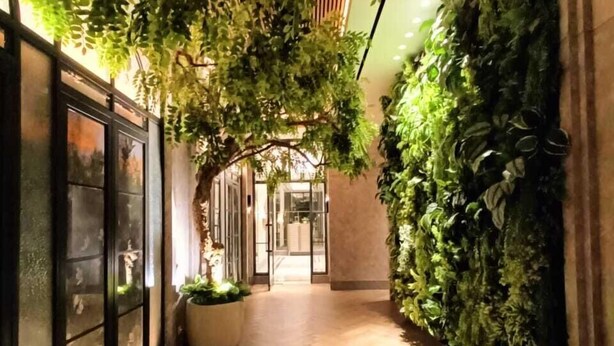 A corridor with a wooden floor, glass doors, and a wall covered in green plants. - Apartmen Pakuwon Bekasi by Ruang Singgah (Bekasi)