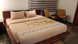 Un letto rifatto con cura, coperta beige e cuscini, un elegante ricamatore in pizzo e fiori gialli.