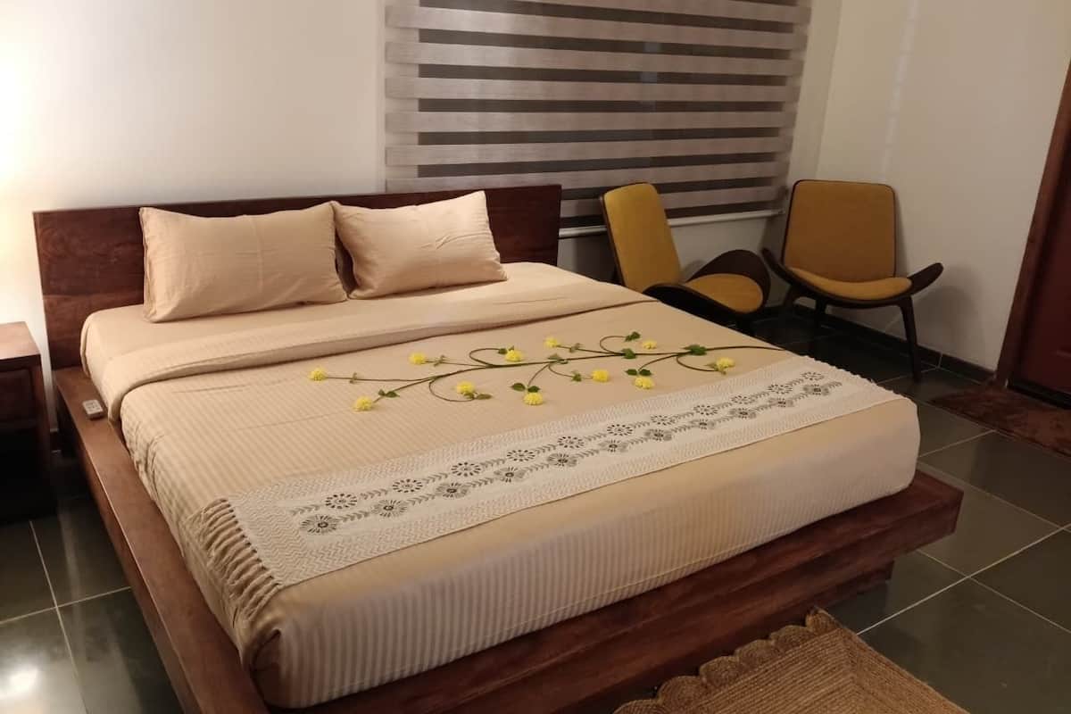 A neatly made bed with a beige bedspread and pillows, a decorative lace runner, and yellow flowers on the bed.