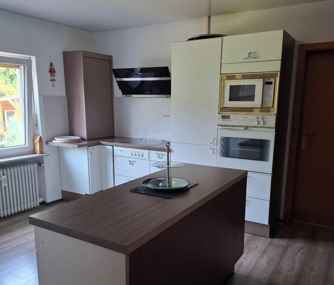 A modern kitchen with white cabinets, a central island, a microwave, and an oven.
