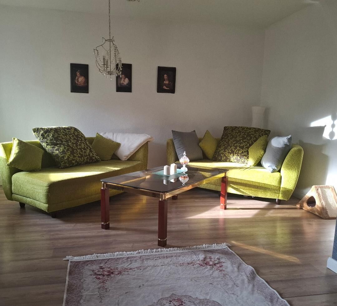 Ein Wohnzimmer mit zwei grünen Sofas, einem Glastisch und Holzboden.