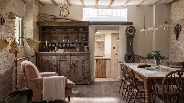 Un coin repas rustique avec une table et des chaises en bois, un lustre ancien et un mur en pierre.