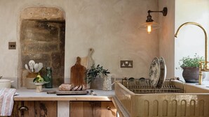 Une cuisine rustique avec un comptoir en bois, une arche en pierre, un luminaire suspendu et un évier doté d’un robinet en laiton.