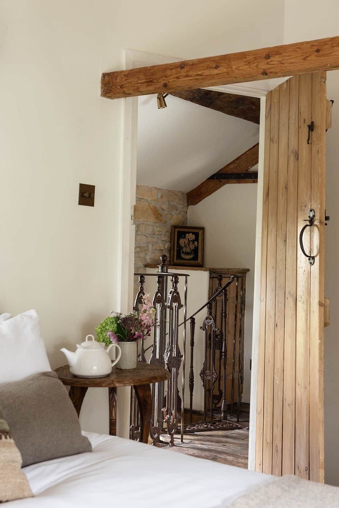 A bedroom with a bed, a white teapot, a vase with flowers, and a rustic wooden door.