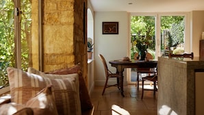 Una sala de estar acogedora con un sofá, una mesa de comedor con sillas y vistas al verdor a través de las ventanas.