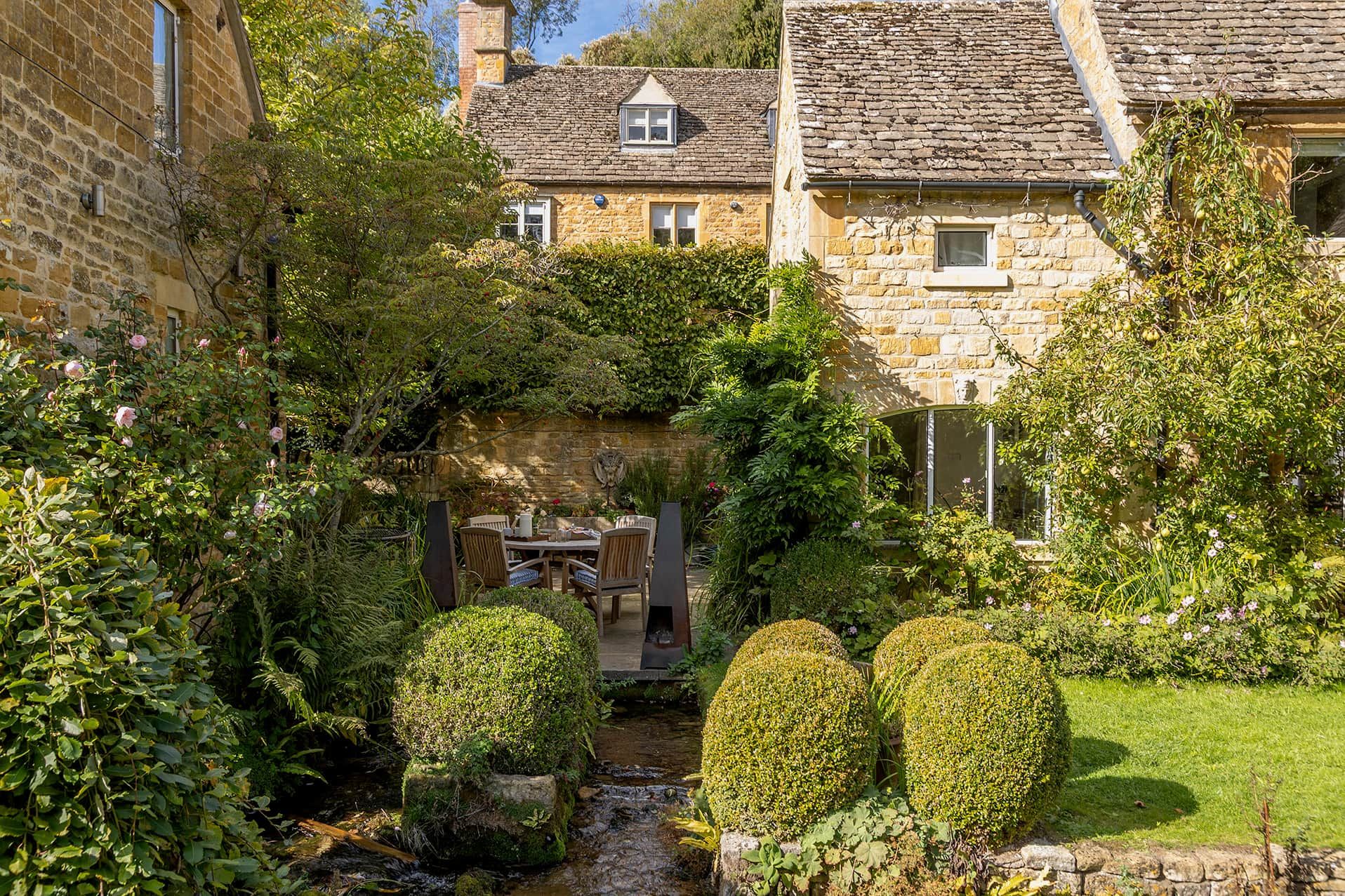 A stone building with a garden, a small stream, and a seating area.