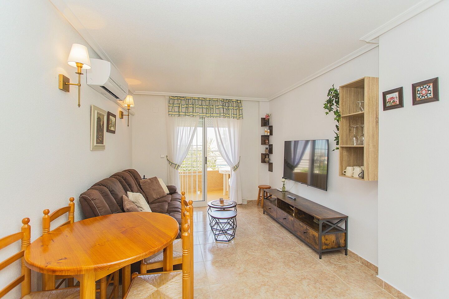 A living room with a sofa, wooden dining table, chairs, a TV, and a small coffee table.