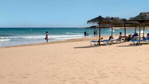 Ein Strand mit Reetdachschirmen und Liegestühlen.