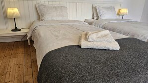 Una habitación de hotel con dos camas, cada una con cabecero blanco y almohadas a juego. Hay dos lámparas de noche a cada lado de las camas.