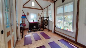 Un estudio de yoga con pisos de madera, colchonetas moradas, techo de vigas de madera y ventanas amplias.