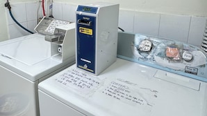 Un espace buanderie équipé d’un lave-linge, d’un sèche-linge et d’un chauffe-eau. Les instructions d’utilisation sont affichées sur le sèche-linge.