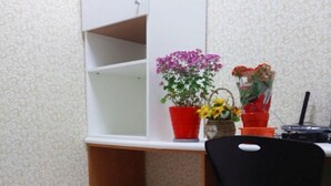 Une petite pièce avec un lit simple, un bureau avec une chaise et deux plantes en pot.