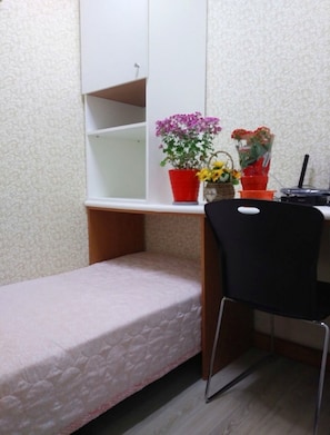 Une petite pièce avec un lit simple, un bureau avec une chaise et deux plantes en pot.