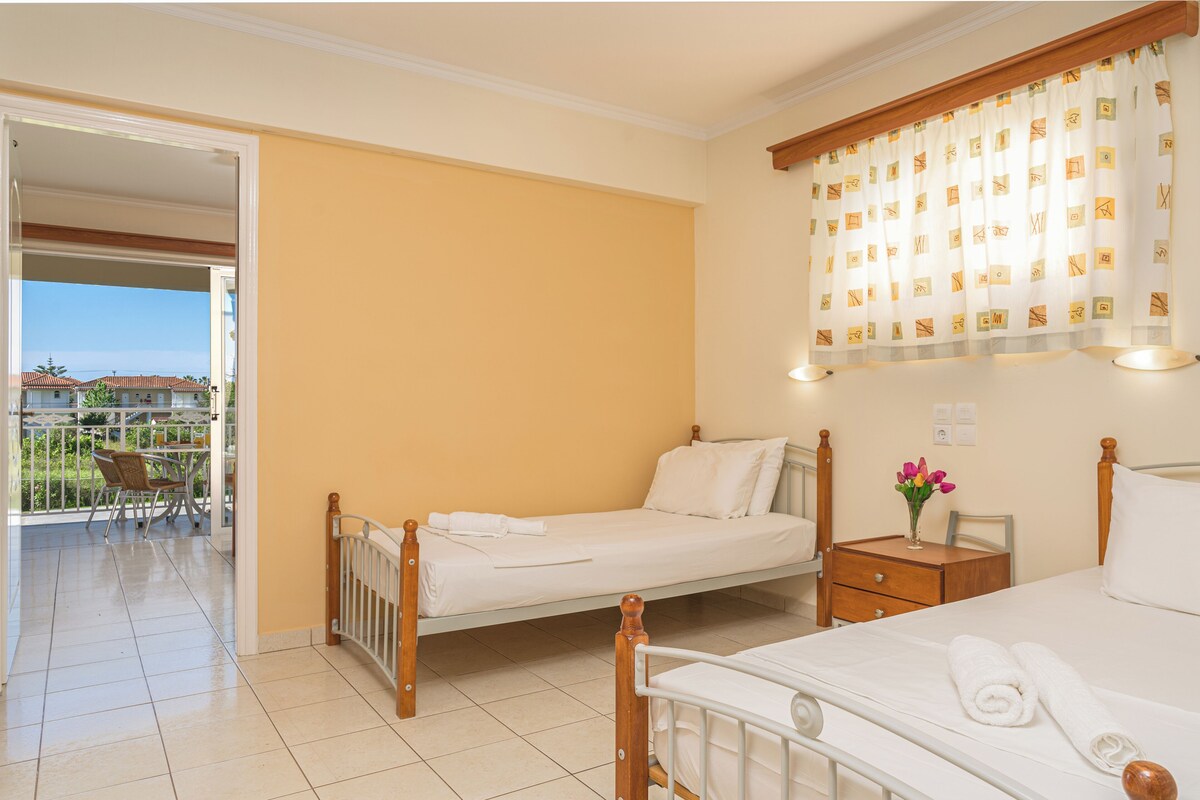 Ein Hotelzimmer mit Balkon, einem Bett, einem Nachttisch und einem fenster mit Vorhängen.