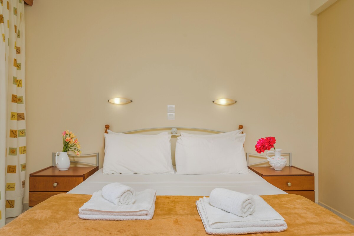 Ein Hotelzimmer mit einem Bett, zwei Nachttischen, einer Nachttischlampe, einer Vase mit Blumen und Handtüchern.