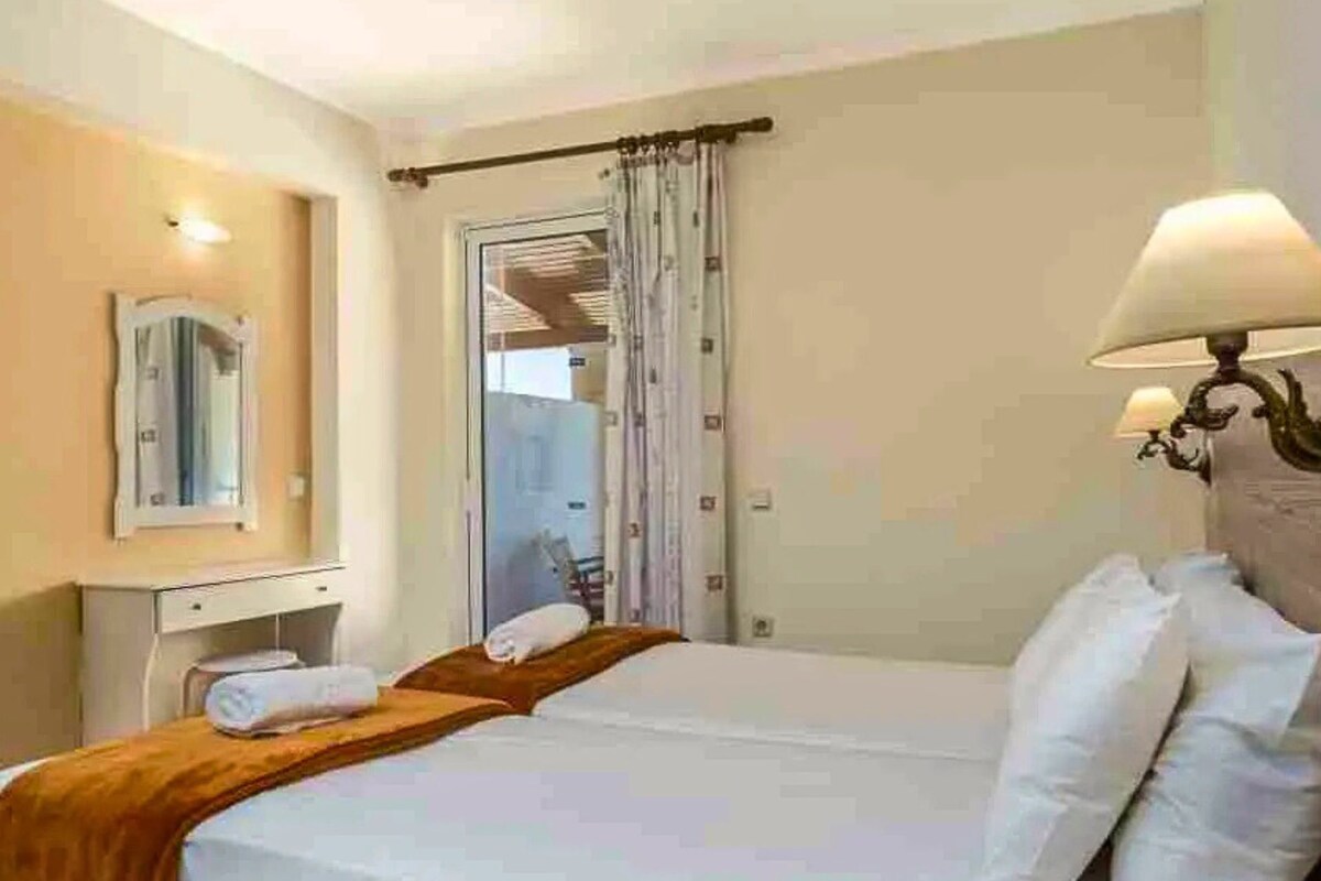 Ein Hotelzimmer mit Bett, Nachttisch, Lampe, Spiegel und einem Fenster mit Vorhängen.