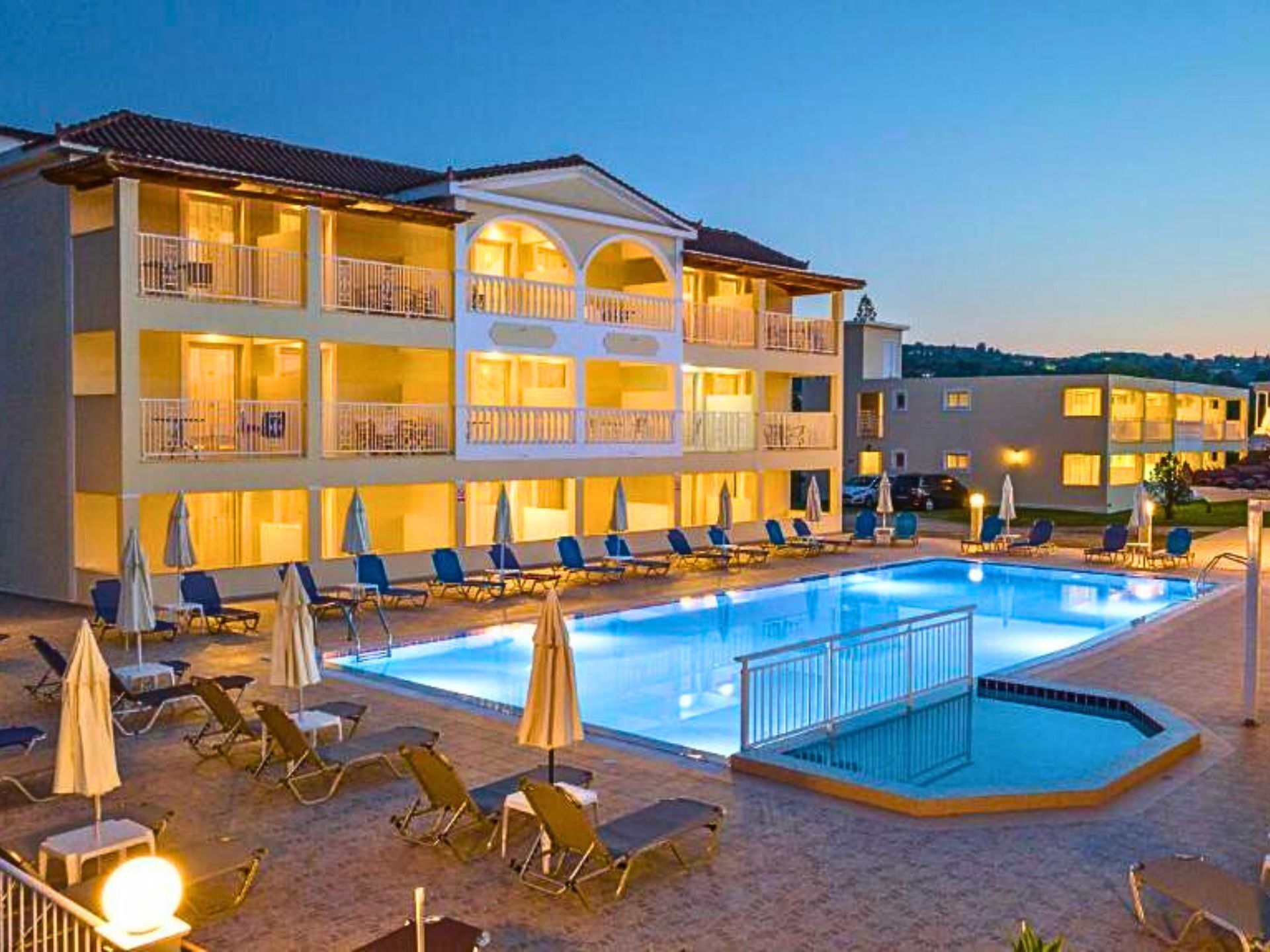 A hotel with a swimming pool, multiple balconies, and sun loungers.