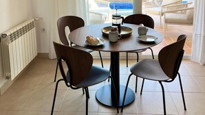 Un área de comedor con una mesa redonda, cuatro sillas, una cafetera y una bandeja con una taza y un plato de comida.
