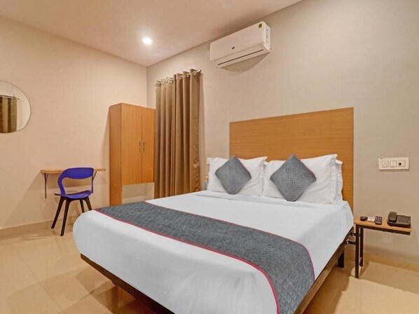 Ett hotellrum med en säng, ett skrivbord, en stol, en luftkonditioneringsanläggning och en telefon.