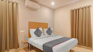 A hotel room with a bed, curtains, an air conditioning unit, and a nightstand. - White Ridge Hotel-Kphb (Hyderabad)