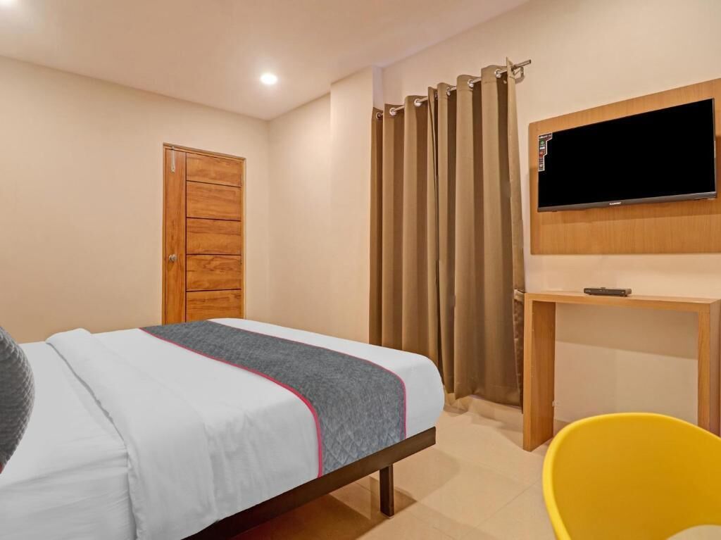 A bedroom with a bed, a wooden wardrobe, a desk with a TV, and a yellow chair.