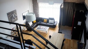 Een moderne woonkamer met een zwart hoekbank, een witte salontafel en een groot raam met gordijnen.