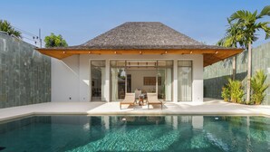 Una casa moderna con piscina, grandes puertas de vidrio y techo de madera sobre un patio.