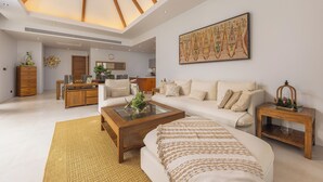 Un salon spacieux avec un plafond haut, un grand tableau, une table basse en bois et un canapé agrémenté d’un plaid à motifs.