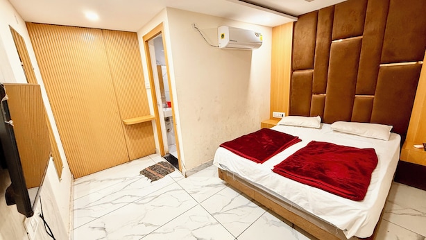 A bedroom with a bed, a wooden wardrobe, an air conditioning unit, and a bathroom door. - Hotel A Grand near All Main Places  (Ujjain)