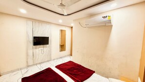 A hotel room with a bed, a flat-screen TV mounted on the wall, an air conditioning unit, and a marble-tiled floor. - Hotel A Grand near All Main Places  (Ujjain)