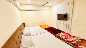 A small, single-bed room with a headboard, a flat-screen TV mounted on the wall, and a power outlet. - Hotel A Grand near All Main Places  (Ujjain)
