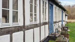 A traditional half-timbered house with white and dark timber framing, a blue door, and a small porch with steps and potted plants. - 4 Star Holiday Home in Rudkobing (Hovborg)